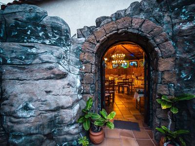 Arco in pietra con piante che conduce a un interno accogliente e ben illuminato di un hotel o ristorante.