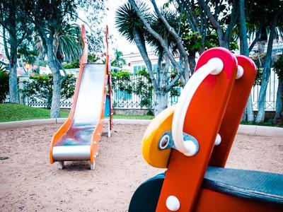 Un gioco per bambini rosso e uno scivolo in metallo su un'area giochi sabbiosa in un parco.