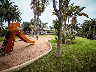 Un parco giochi con uno scivolo arancione e palme in un'area verde.
