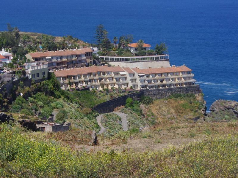 Hotel su una collina costiera con vista sul mare blu circondato da vegetazione.