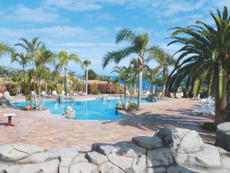 Piscina dell'hotel con palme e sdraio sotto il cielo azzurro