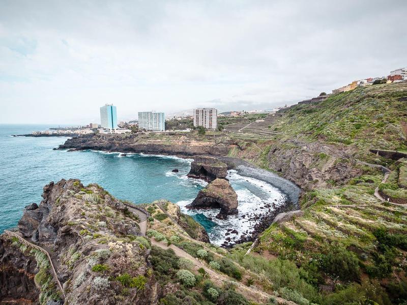 Paesaggio costiero con rocce, onde e edifici sullo sfondo sotto un cielo nuvoloso