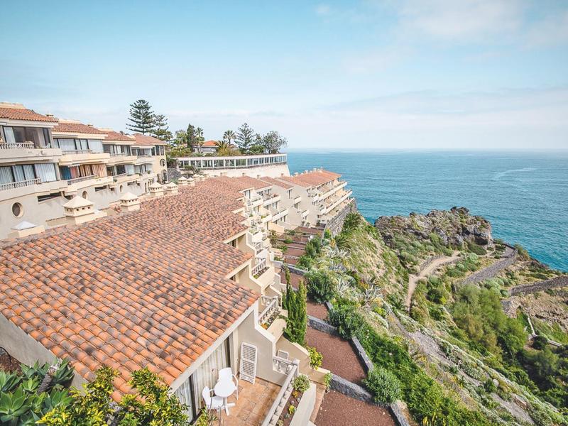 Edifici dell'hotel con tetti in tegole rosse su una scogliera rocciosa con vista sul mare.