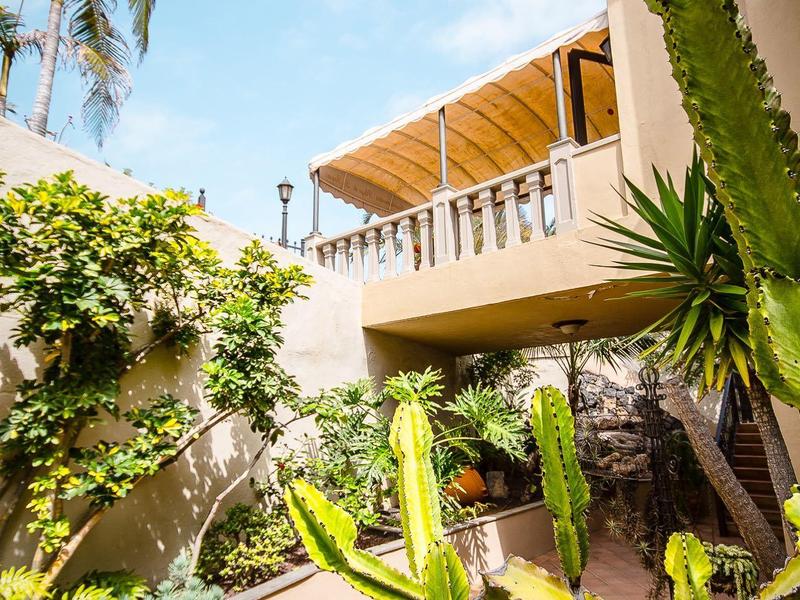 Un cortile soleggiato con cactus e palme davanti a un edificio dell'hotel con balcone.