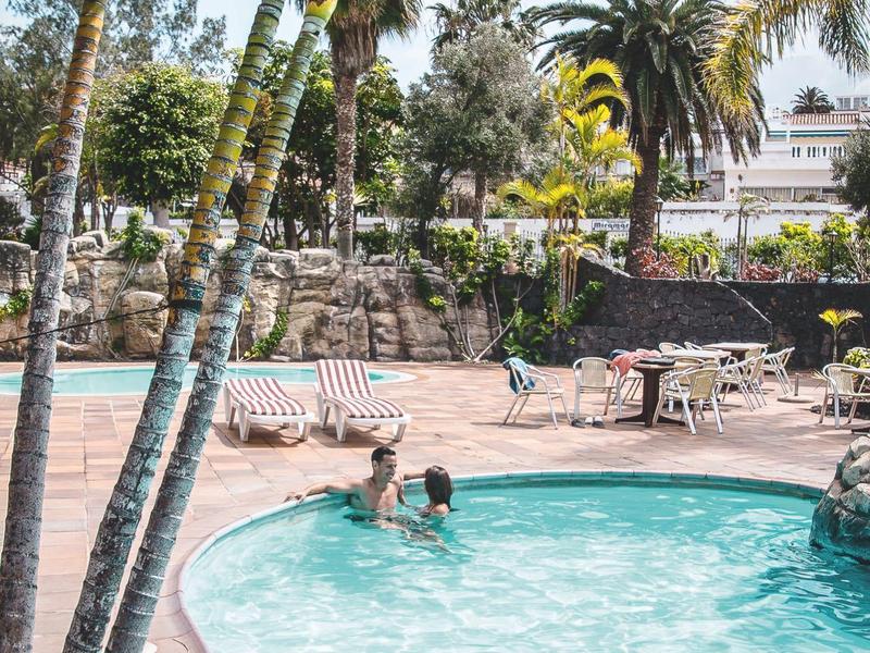 Piscina all'aperto con persone e palme in un'area dell'hotel alla luce del sole.