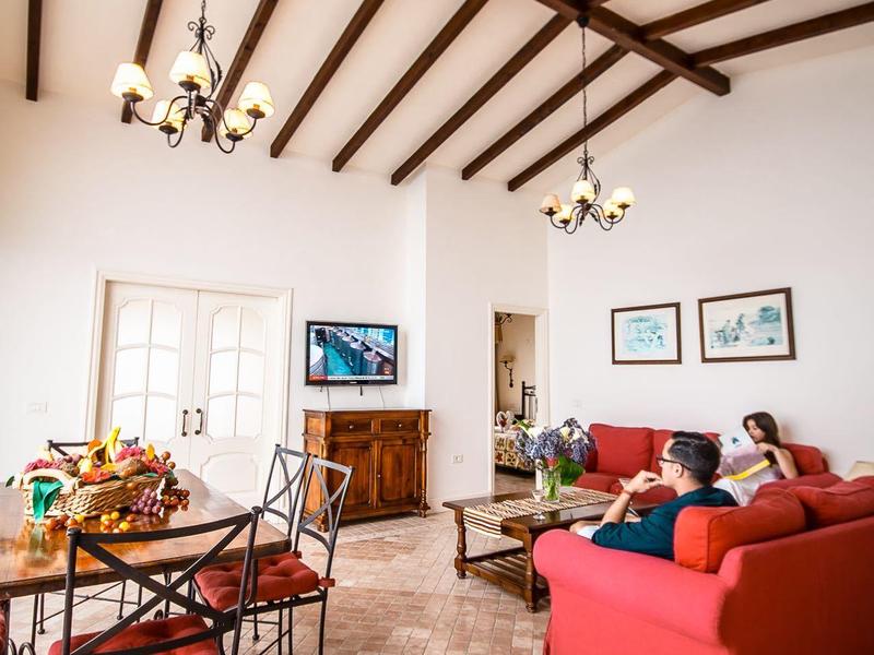 Soggiorno luminoso con divani rossi, mobili in legno e travi a vista sul soffitto.