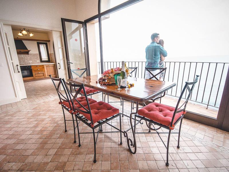Sala da pranzo con tavolo in legno, sedie rosse e un uomo sul balcone.