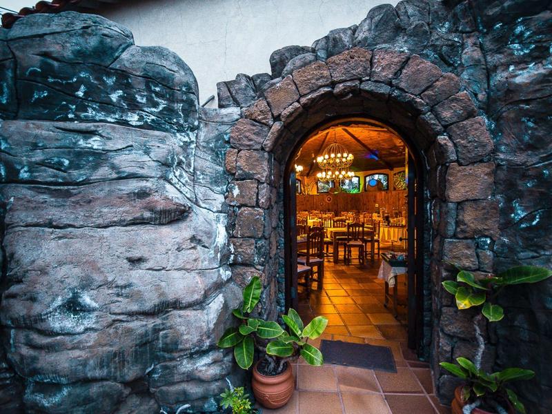 Arco in pietra con piante che conduce a un interno accogliente e ben illuminato di un hotel o ristorante.