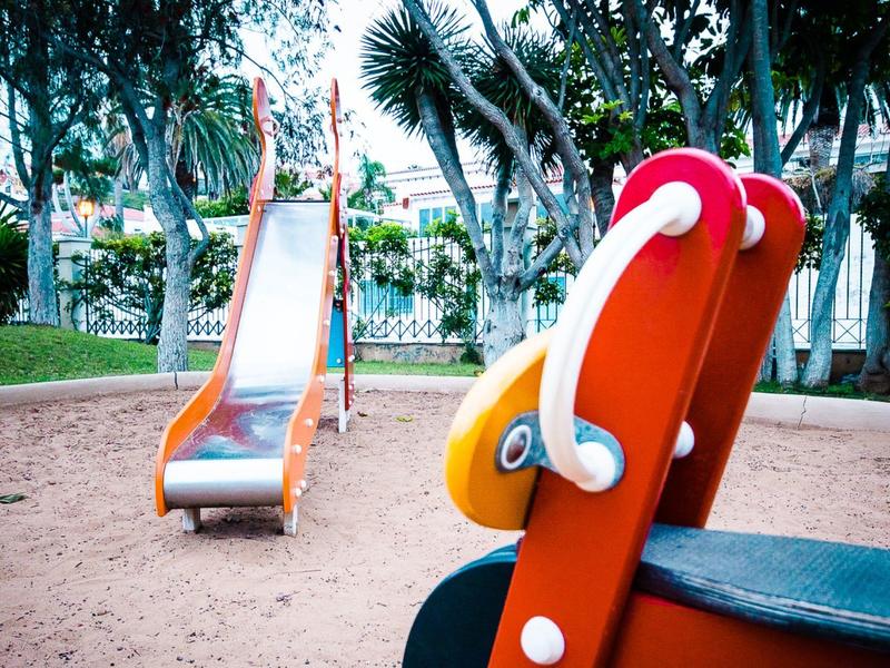 Un gioco per bambini rosso e uno scivolo in metallo su un'area giochi sabbiosa in un parco.