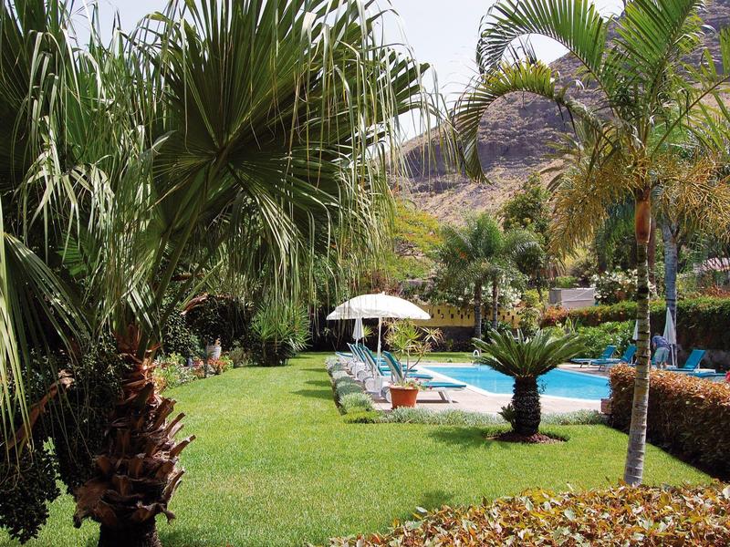 Grüner Garten mit Palmen und Swimmingpool in einer Hotelanlage unter strahlendem Himmel.
