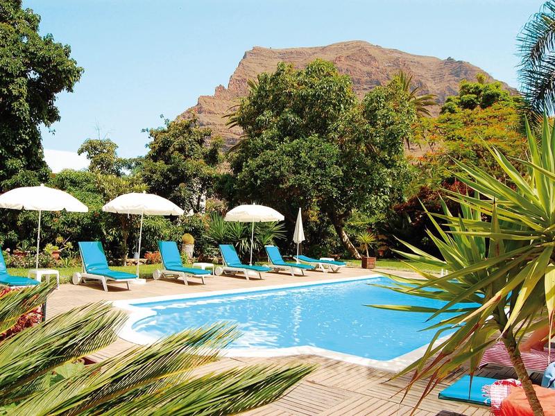 Pool mit blauen Liegestühlen und Sonnenschirmen vor einer Bergkulisse im Hotelgarten.