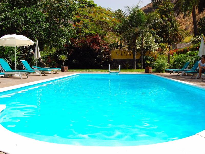 Klares blaues Schwimmbad mit Liegestühlen und Sonnenschirmen im Gartenbereich.