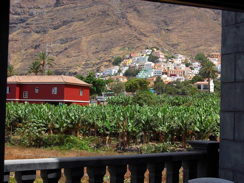 Blick von einem Balkon auf ein grünes Feld und bunte Häuser an einem Berghang.