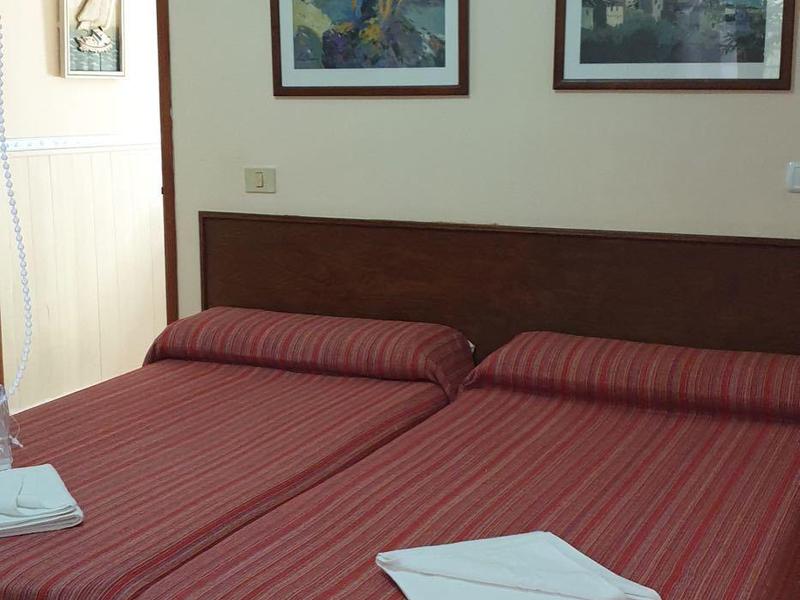 Hotelzimmer mit zwei Einzelbetten, rot gestreiften Bettdecken und zwei Bildern an der Wand.