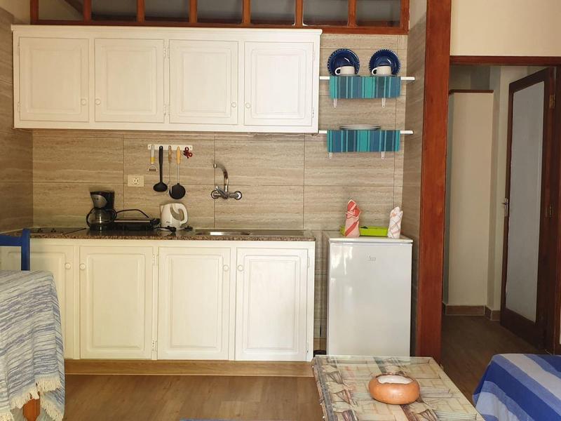 Küche mit weißen Schränken, Spüle, Kaffeemaschine und kleinem Tisch mit Stühlen in einem gemütlichen Raum.