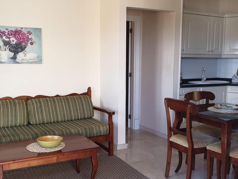 Gemütlicher Wohn- und Essbereich mit grünem Sofa, Holztisch und Küchenzeile.