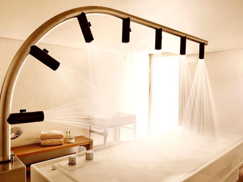 Světlá spa místnost s dešťovými sprchami nad masážním stolem a ambientním osvětlením.