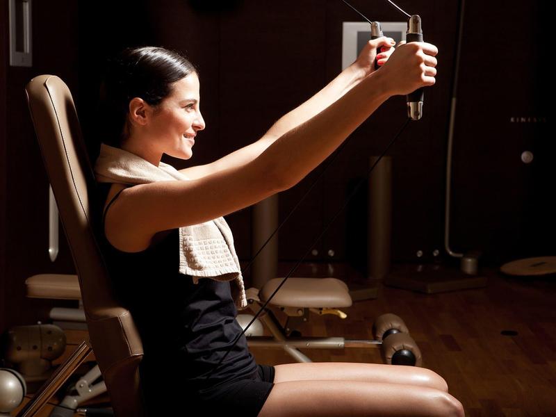 Žena cvičí na veslovacím stroji v tmavé posilovně s dřevěnou podlahou.