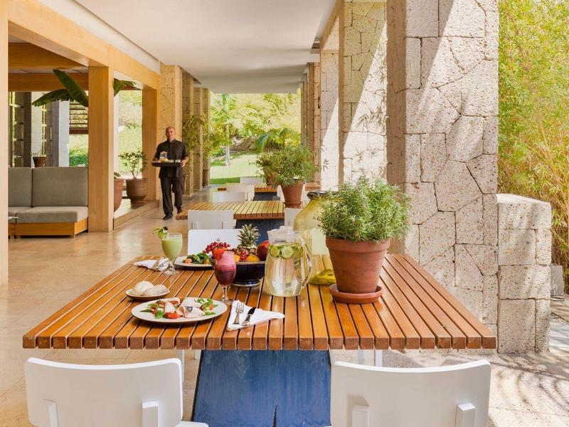 Venkovní posezení s dřevěným stolem, nápoji a občerstvením na slunné terase.