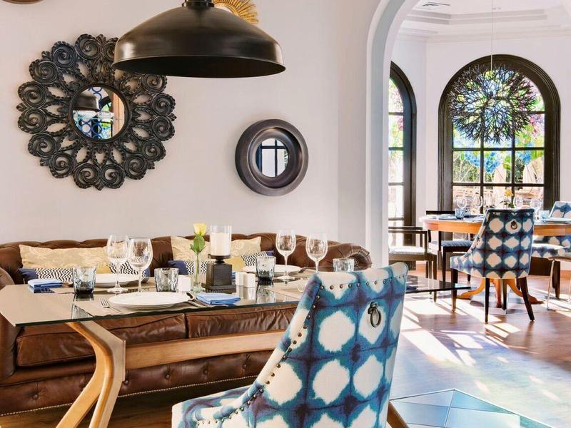 Elegantní jídelní prostor se dřevěným stolem, modrou vzorovanou židlí, černo-bílými dlaždicemi a obloukovými okny