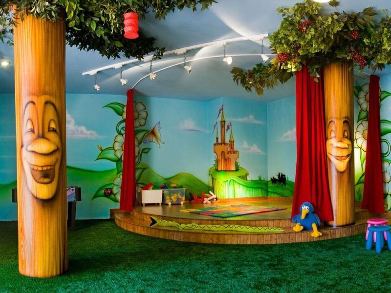 Barevná vnitřní dětská herna se stromy, kreslenými nástěnnými malbami a malými židlemi.