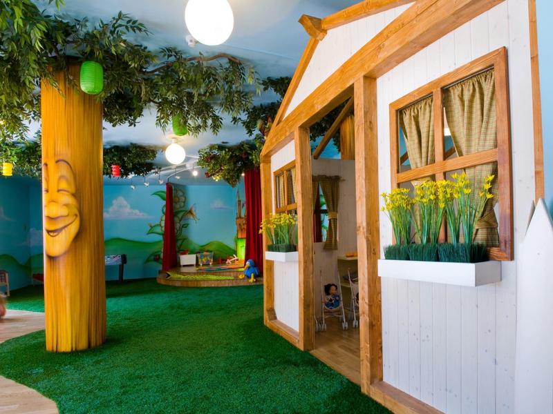 Pohodlná vnitřní herní plocha s dřevěným domečkem, umělou trávou a závěsnými světly.