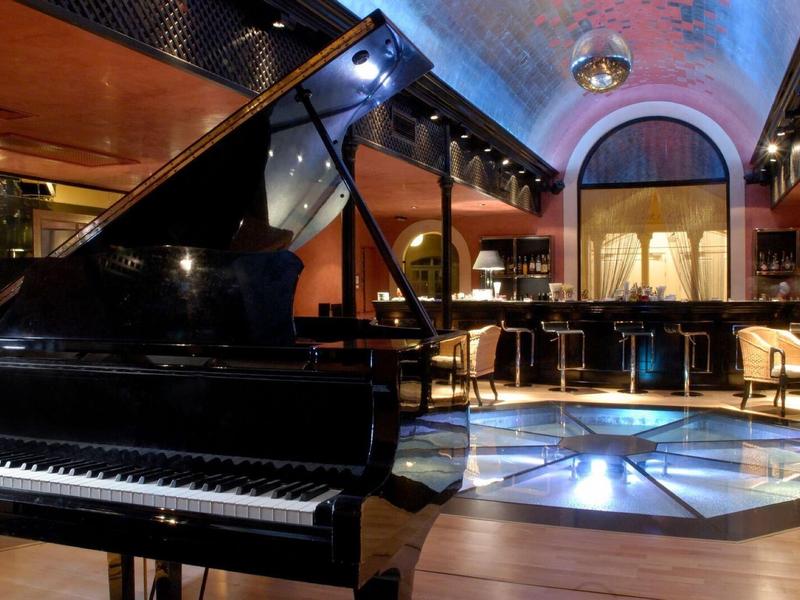 Elegantní hotelový salonek s křídlem, moderním osvětlením a stylovou posezením.