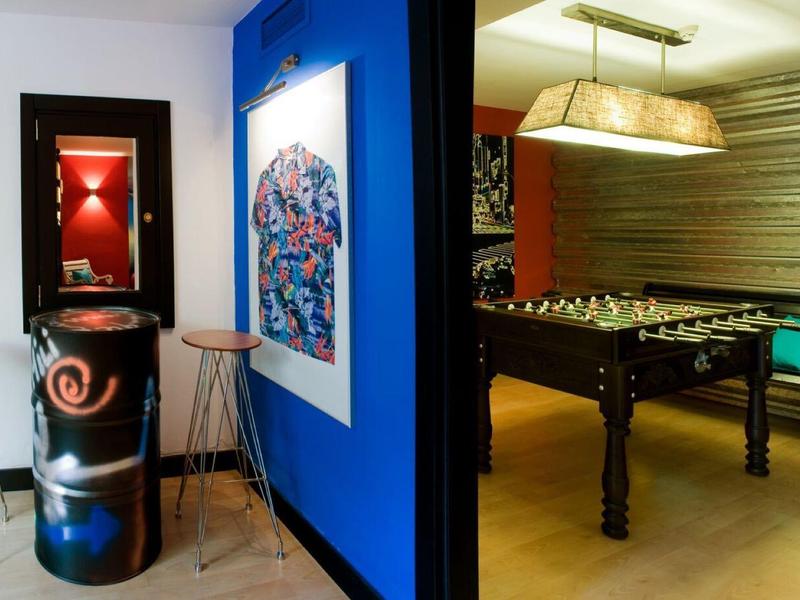 Moderní vnitřní herna s fotbálkem, stoličkami a barevným nástěnným uměním.