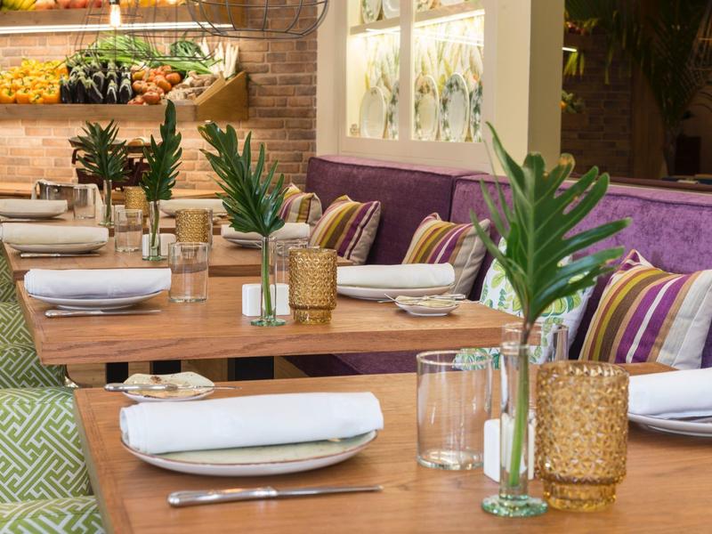 Příjemná restaurace s dřevěnými stoly, fialovým posezením a zelenými rostlinami na stolech.