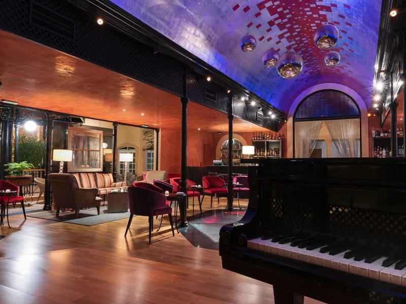 Hotelový salón s pianem, barevným stropem, moderním nábytkem a atmosférickým osvětlením.