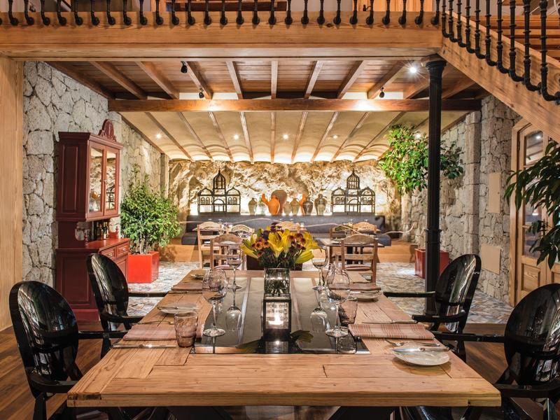 Rustikální jídelní prostor s dřevěným stolem, černými židlemi a kamennými zdmi v útulném prostředí.