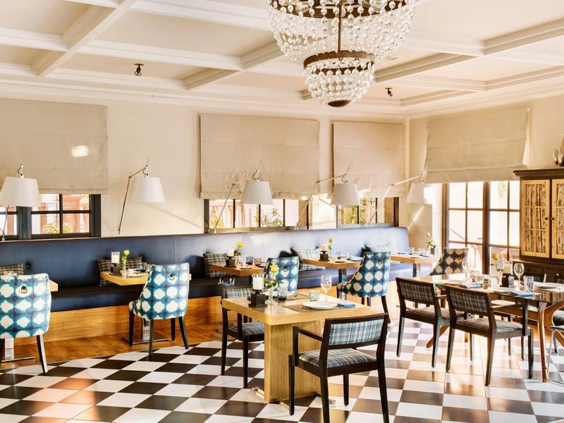 Elegantní jídelna s šachovnicovou podlahou, vzorovanými židlemi, dřevěnými stoly a jemným osvětlením.