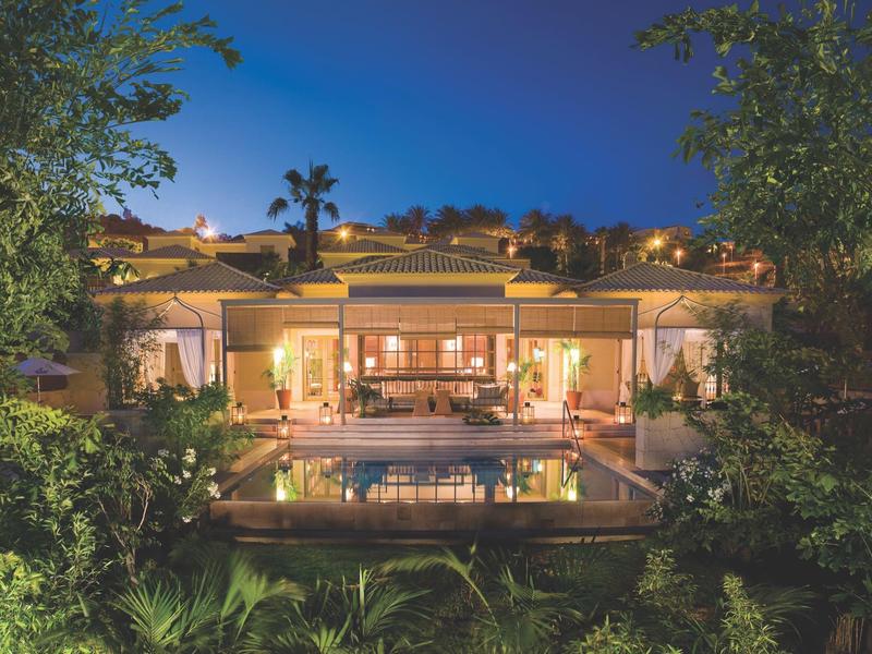 Luxusní vila za soumraku s bazénem obklopená bujnou zelení a teplým osvětlením.