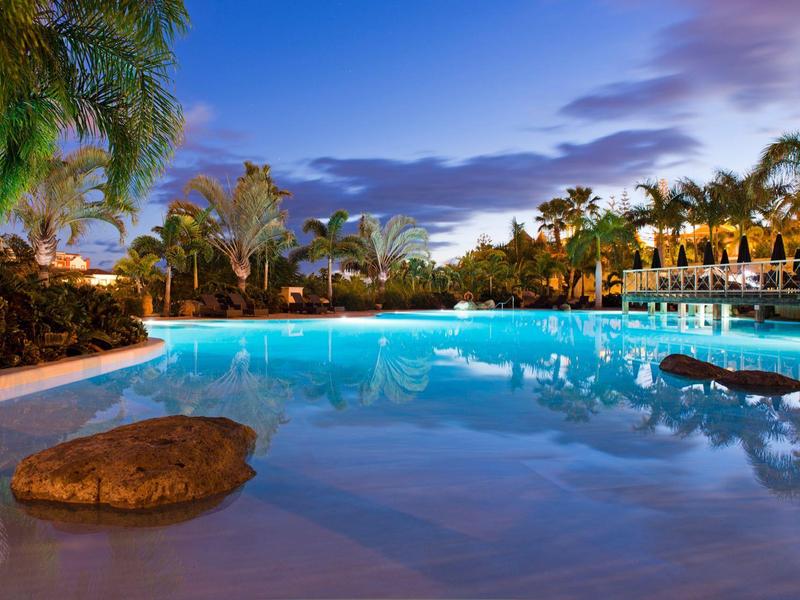 Klidný hotelový bazén za soumraku s palmami a lehátky kolem.