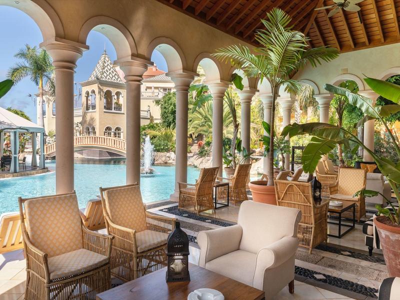 Luxusní posezení u bazénu s oblouky, rostlinami a lehátky v resortu.