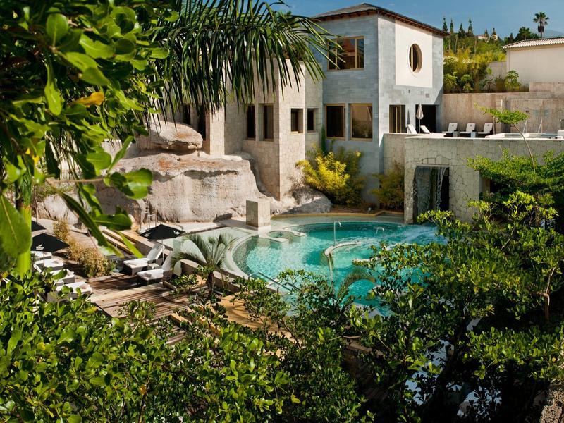 Příjemná vila s bazénem obklopená bujnou zelení a lehátky.