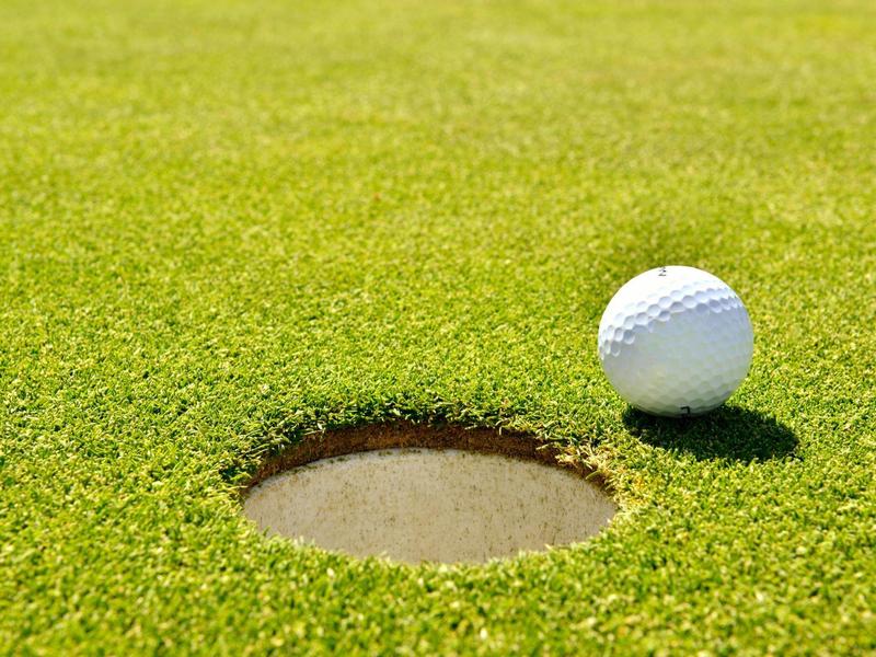 Weißer Golfball liegt neben einem Loch auf gepflegtem, grünem Golfplatz.