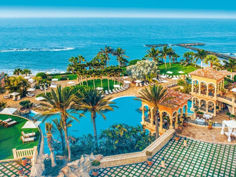 Großer Pool mit Palmen und Liegen am Meer in sonniger Umgebung eines Resorts.