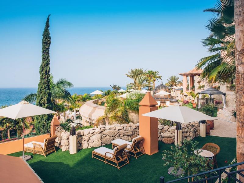 Luxuriöse Terrasse mit Sonnenschirmen, Liegestühlen, Palmen und Meerblick unter blauem Himmel.