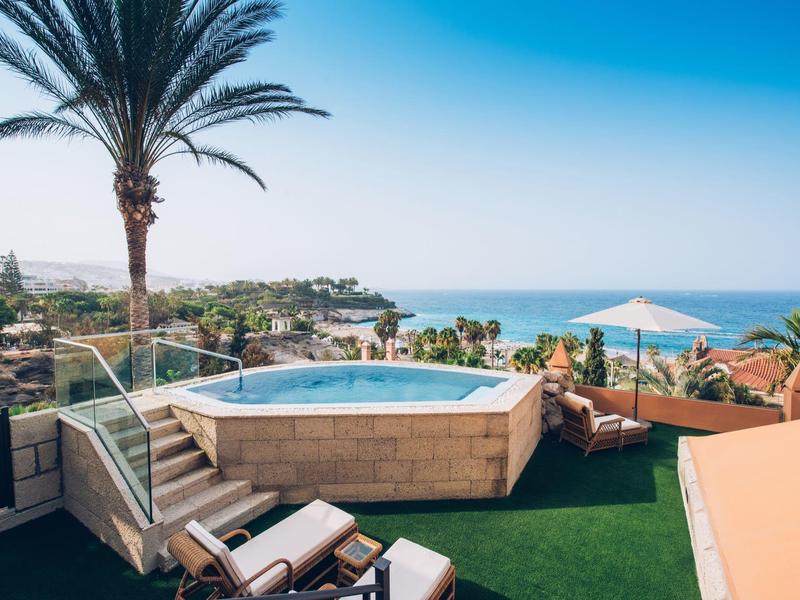 Rundpool auf Terrasse mit Liegestühlen, Palmen und Meer im Hintergrund, blauer Himmel.
