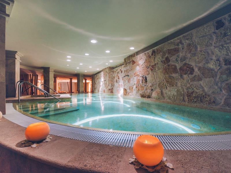 Innenpool mit steinerner Wand, warmem Licht und Kerzen für entspannte Atmosphäre.