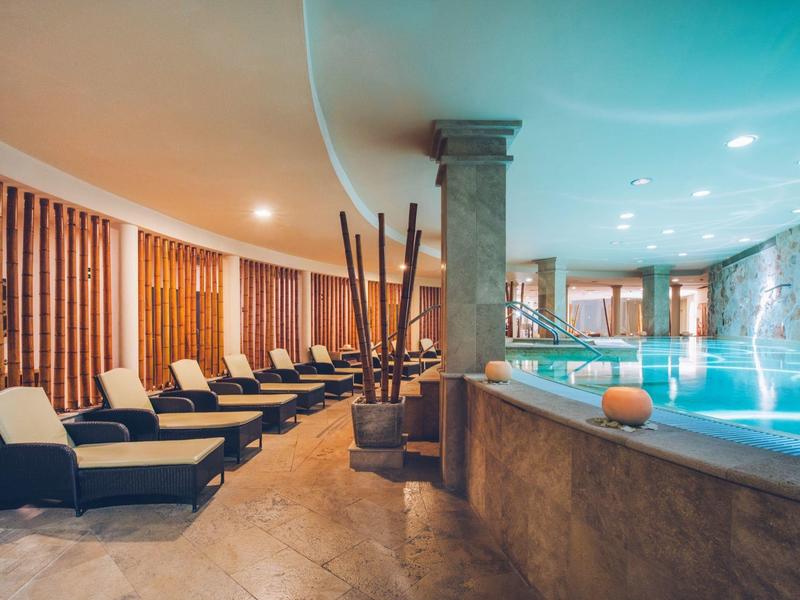 Innenraum eines Wellnesspools mit Liegestühlen, Holzvertäfelung und einem Pfeiler in der Mitte.