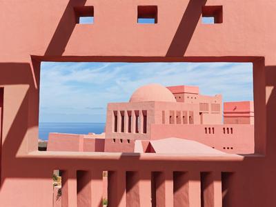 Roze gebouw met raam dat de zee onder een blauwe lucht toont.