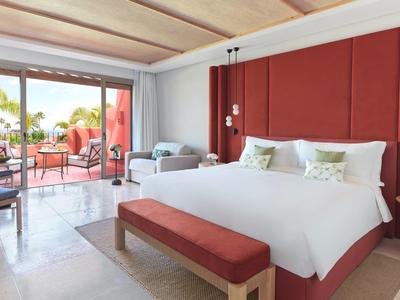 Moderne hotelkamer met groot bed, rode accenten en terras met uitzicht op zee.