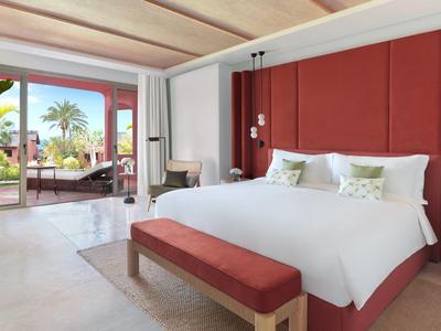 Modern hotelkamer met groot bed, rode accenten en terras met uitzicht op palmbomen