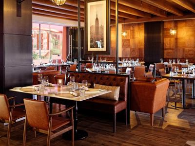Modernes Restaurant mit Holzböden, braunen Ledersesseln, Tischen mit Tischdecken und warmem Licht.