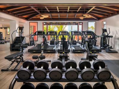 Innenraum eines Fitnessstudios mit Hanteln und verschiedenen Cardiogeräten in hell beleuchtetem Raum.