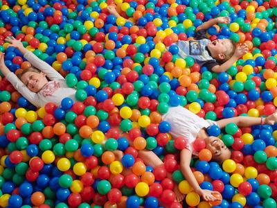 Drei Kinder liegen entspannt in einem großen Becken voller bunter Plastikbälle.