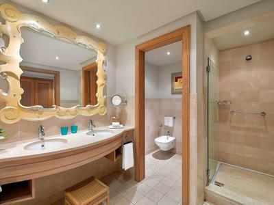 Helles Badezimmer mit Doppelwaschbecken, geschwungenem Spiegel, separater Toilette und Duschkabine.