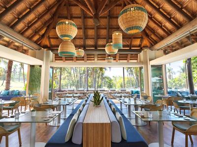 Hell eingerichtetes Restaurant mit Holzstuhl, Glasfenstern und Sicht auf grüne Außenanlage.